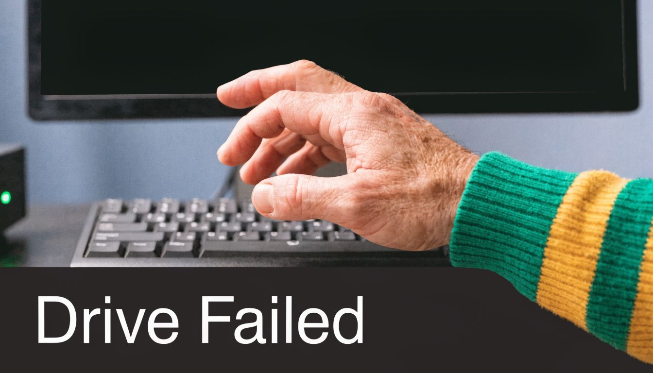 A close-up view of an older person's hand typing on a keyboard with a Drive Failed notification.